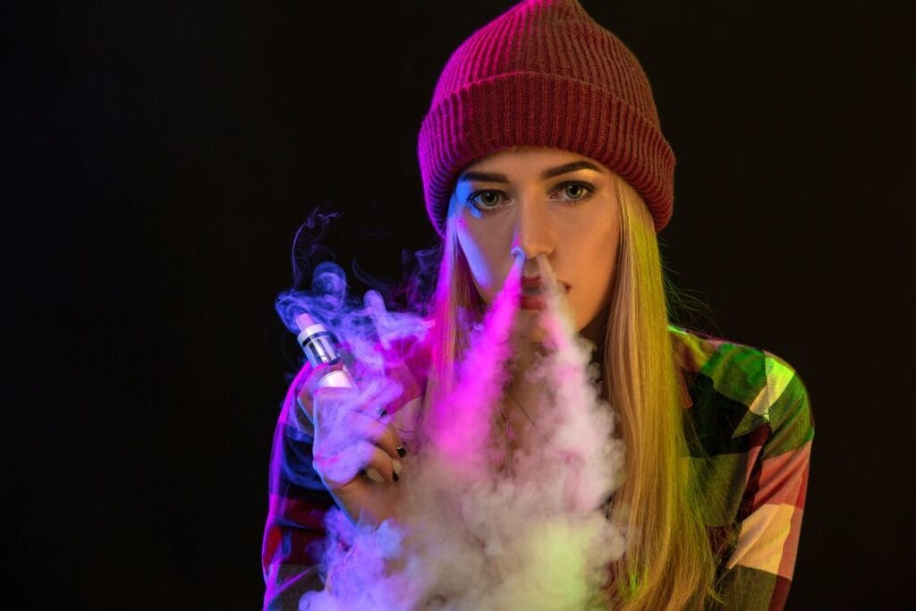 Vaping girl. Young hipster woman vape e-cig on studio on black background. Hip-hop style. Close up.