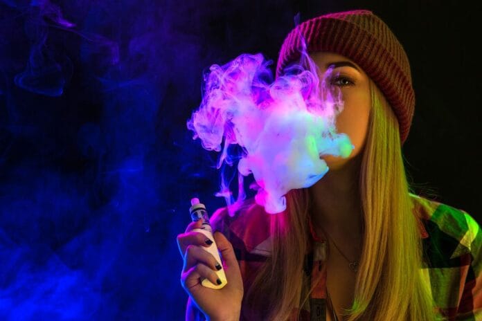 Vaping girl. Young hipster woman vape e-cig on studio on black background. Hip-hop style. Close up.